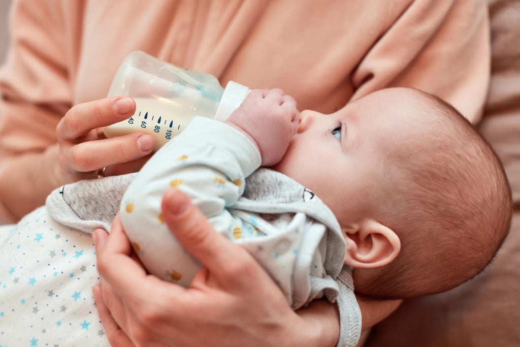 mother feeds her little cute newborn baby with milk bottle at home. Mom takes care of the child.