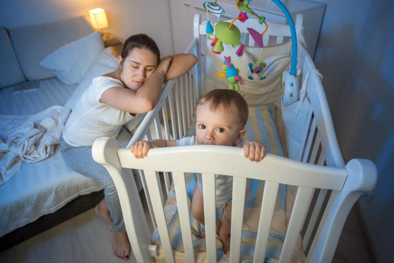 Tired mother got asleep next to baby's crib