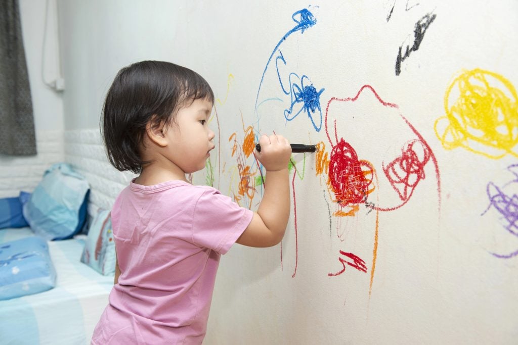 little baby girl drawing with crayon color on the wall