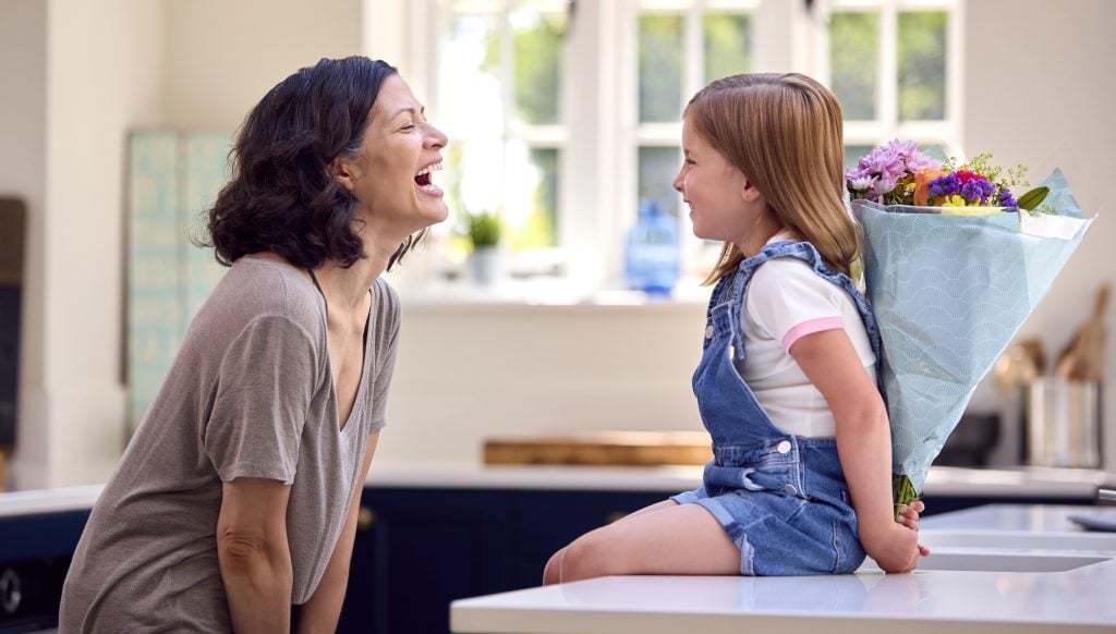 Family At Home With Daughter Giving Older Mother Bunch Of Flowers