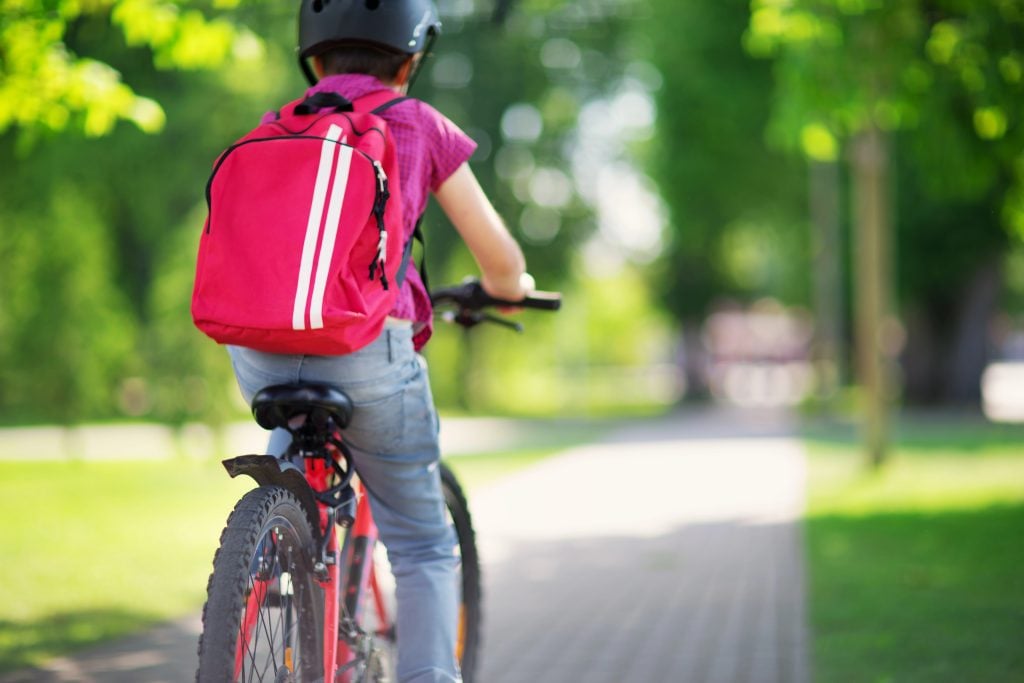 A free range child biking somewhere outside with his backpack.