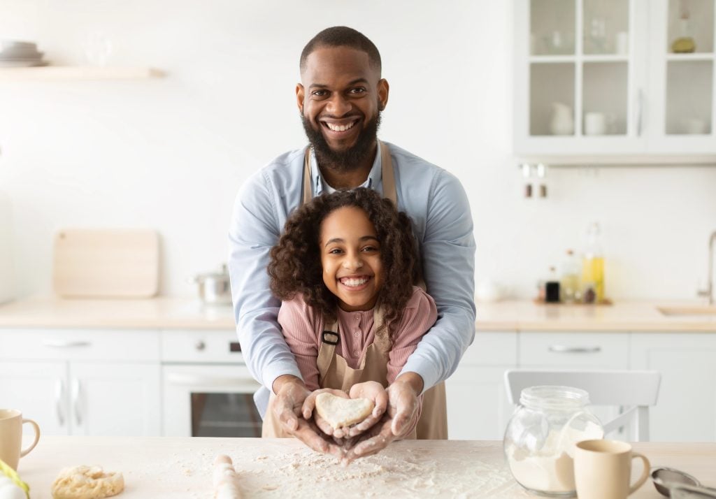 Happy black man and girl holding dough in heart shape