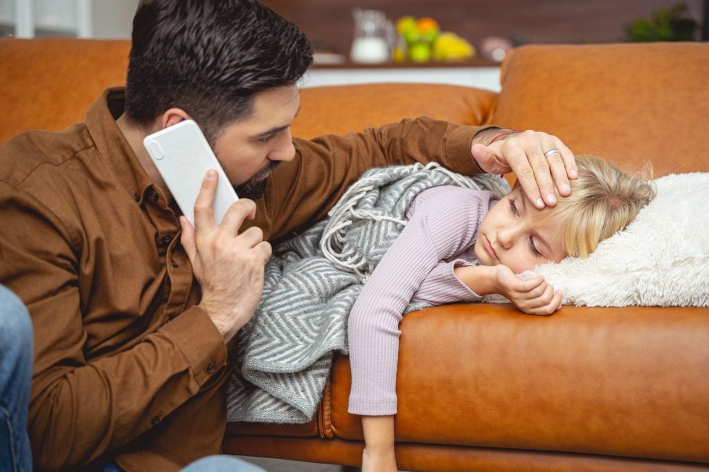 Caring father calling doctor and touching daughter forehead