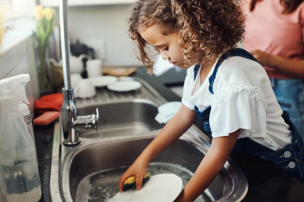 A little girl with strict parents washing the dishes
