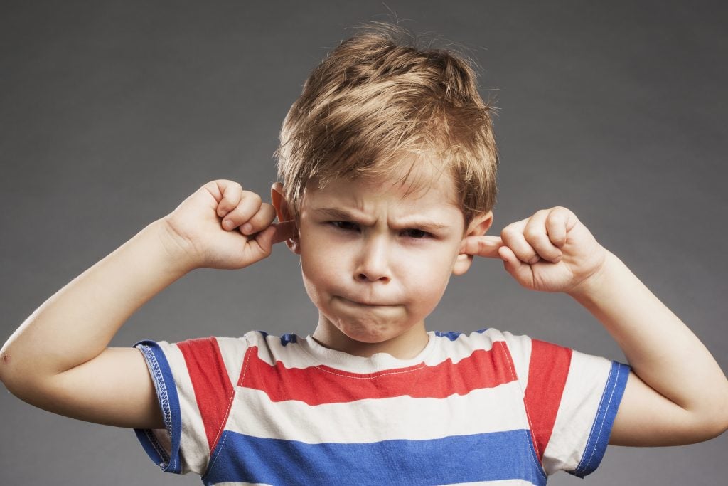 Young boy covering ears against gray background