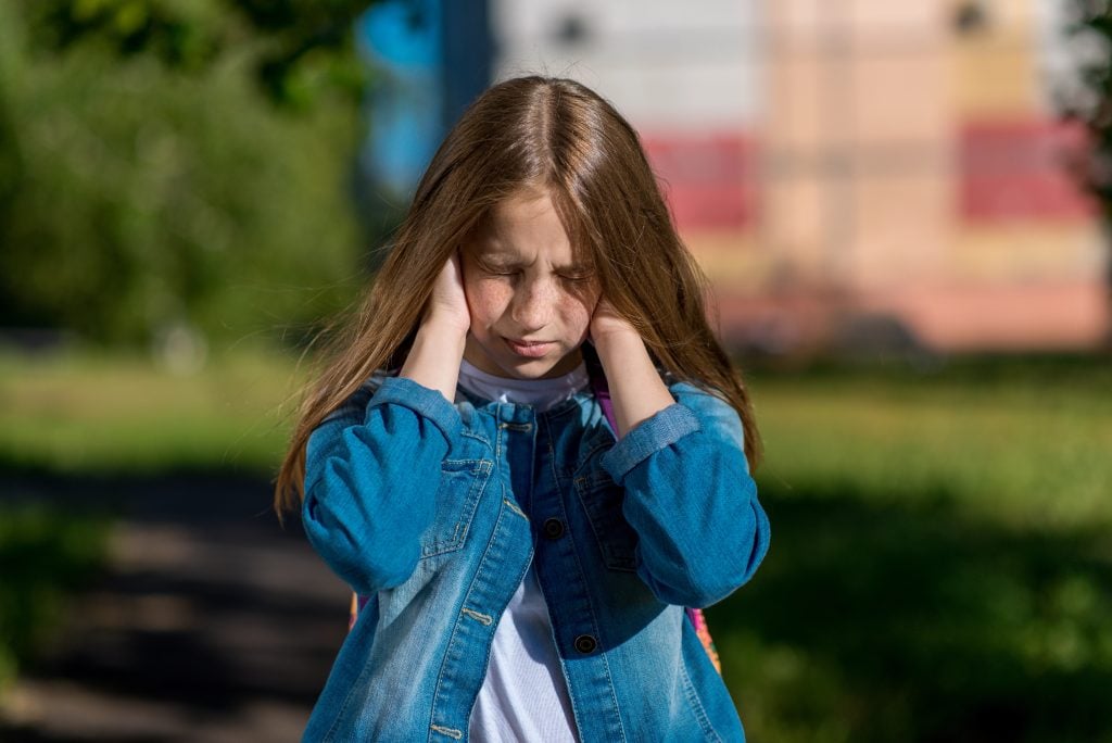Little girl schoolgirl in summer park. He covers his ears with hands. The concept of loud noise, problems in family, scandal, reluctance listen, discontent. Emotions of quarrel, frustration, conflict.