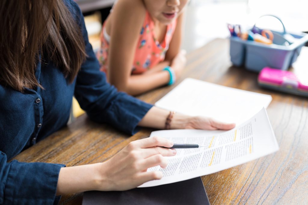 Midsection of mother with school notes teaching daughter at table in home