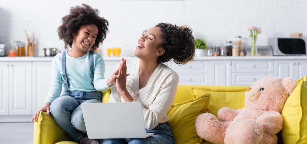 cheerful african american kid with mom giving high five near laptop at home, banner