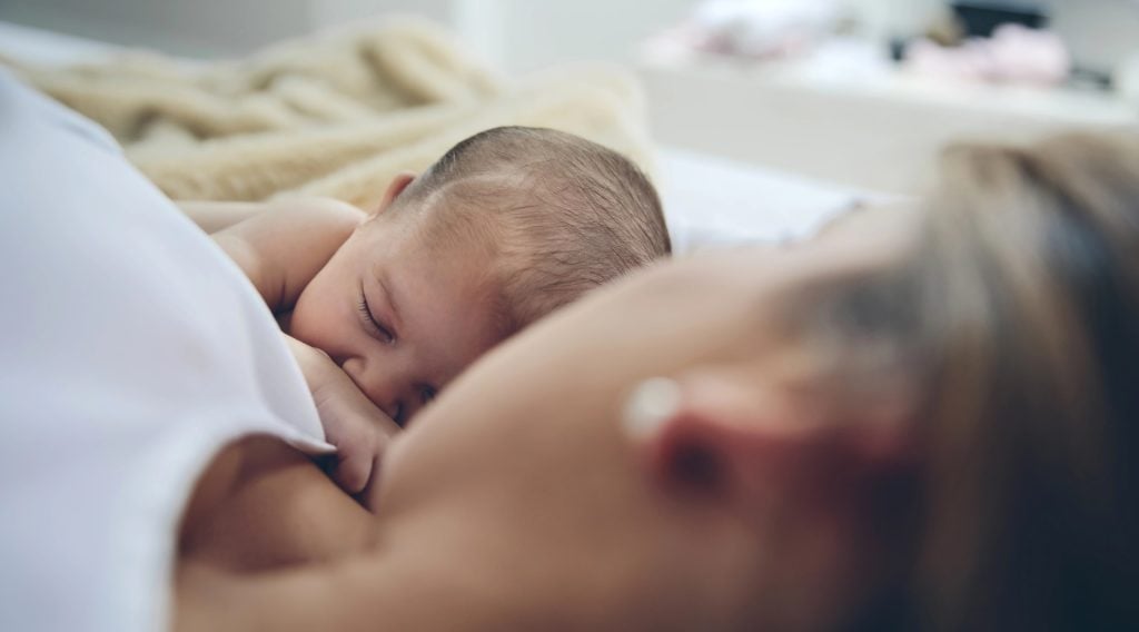 Newborn lying on the bed with her attached mother