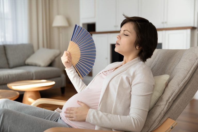Tired pregnant woman use hand fan at home