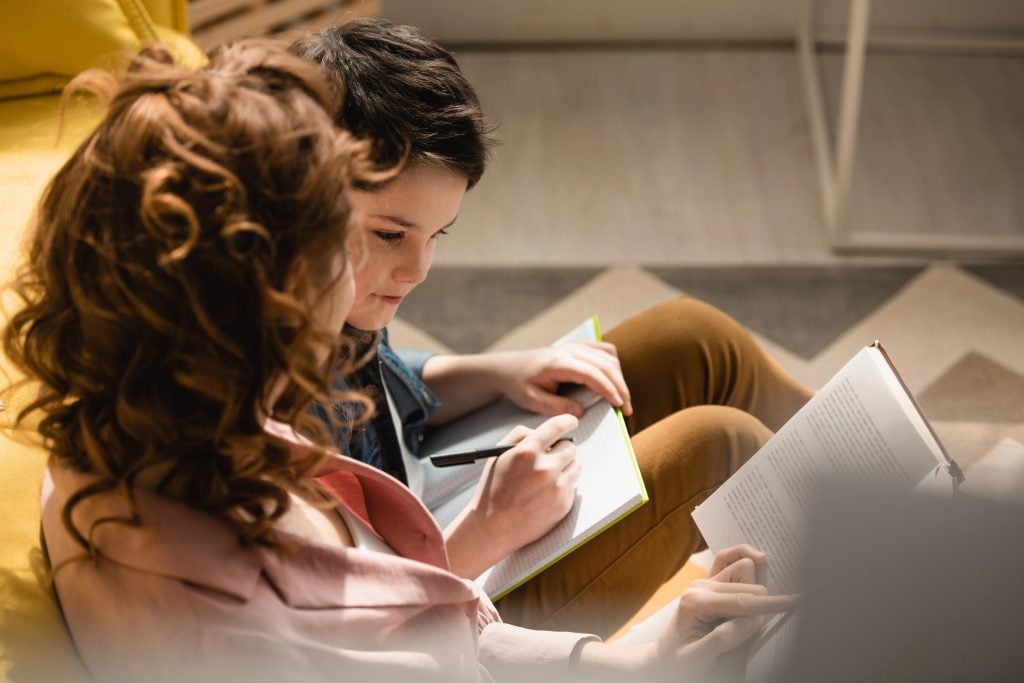 selective focus of mother and son sitting on floor and making homework together at homeschool
