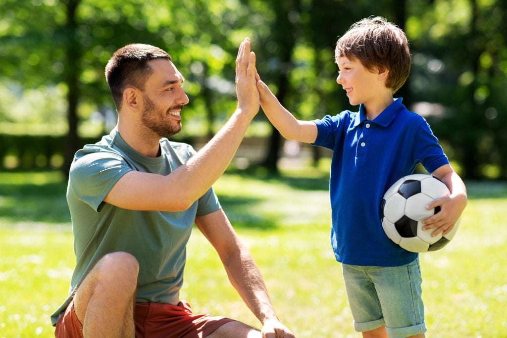 father giving five to son with soccer ball at park