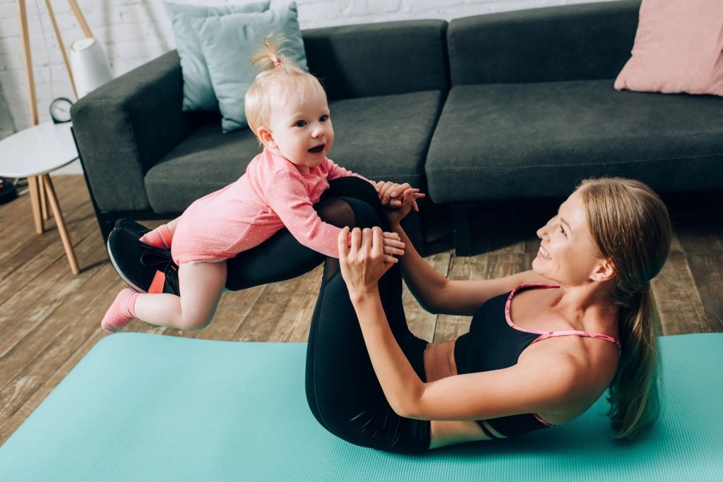 Athletic woman holding baby daughter while working out on fitness mat at home