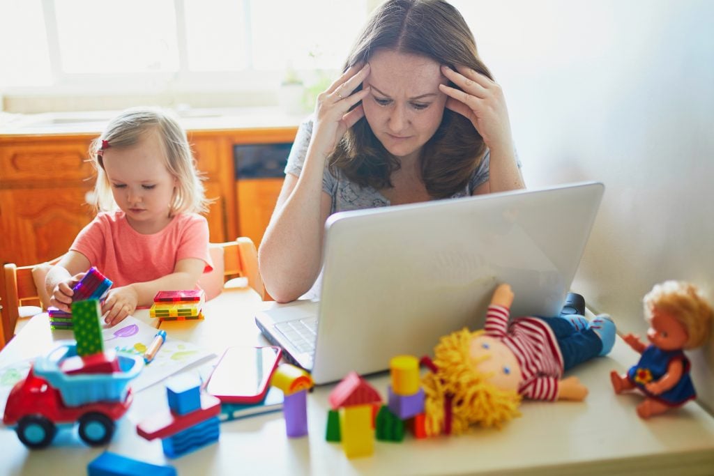 Exhausted and stressed mother working from home with toddler. Quarantine and closed daycare centres during coronavirus outbreak. Child making noise and disturbing woman at work. Freelance job with kid