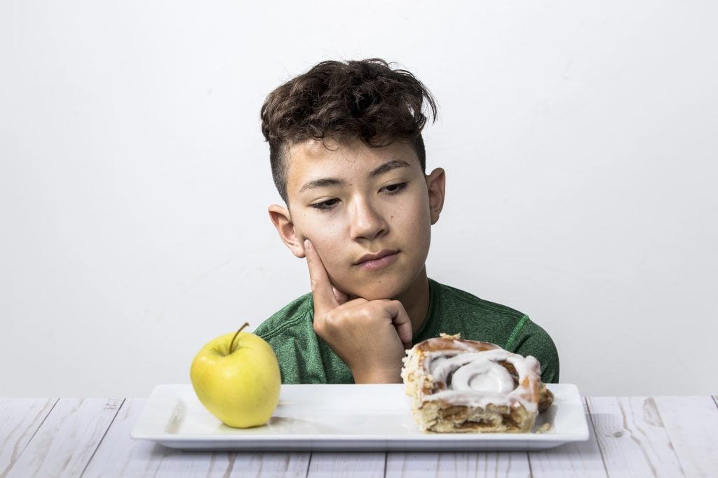 A concept photo of a teen boy trying to decide between a healthy apple and a sweet cinnamon roll.