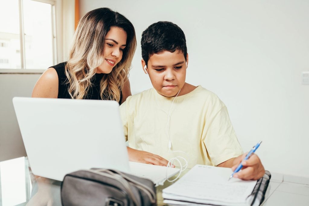 Young student doing homework at home with laptop helped by his mother. Mom teaching his son. Education, family lifestyle, homeschooling concept