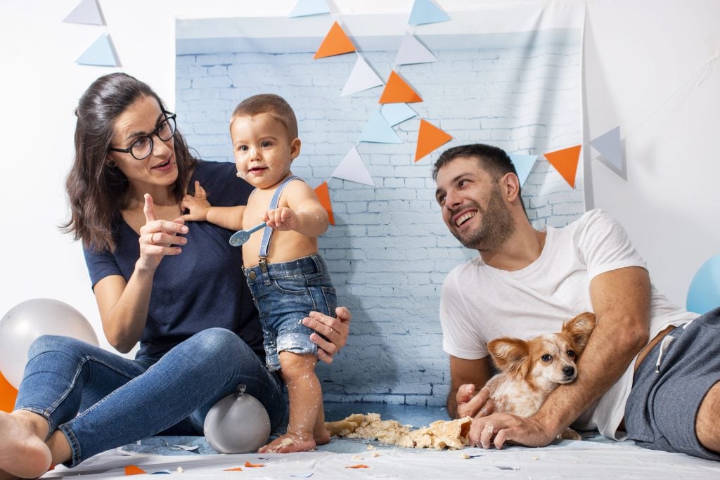 Parents playing with son on party for one year baby boy with a set composed of brick wallpaper.