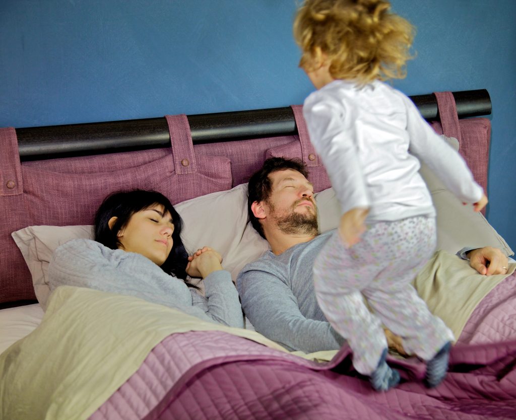 Little girl jumping on bed while parents are sleeping