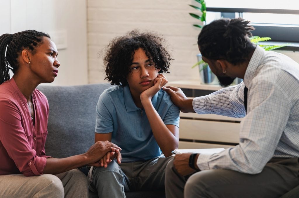 Dr. talking to a teenaged kid about his behaviors, next to his mom