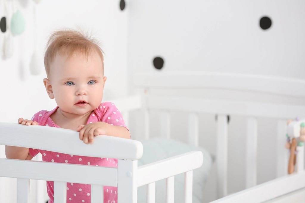 Cute little baby standing in crib at home