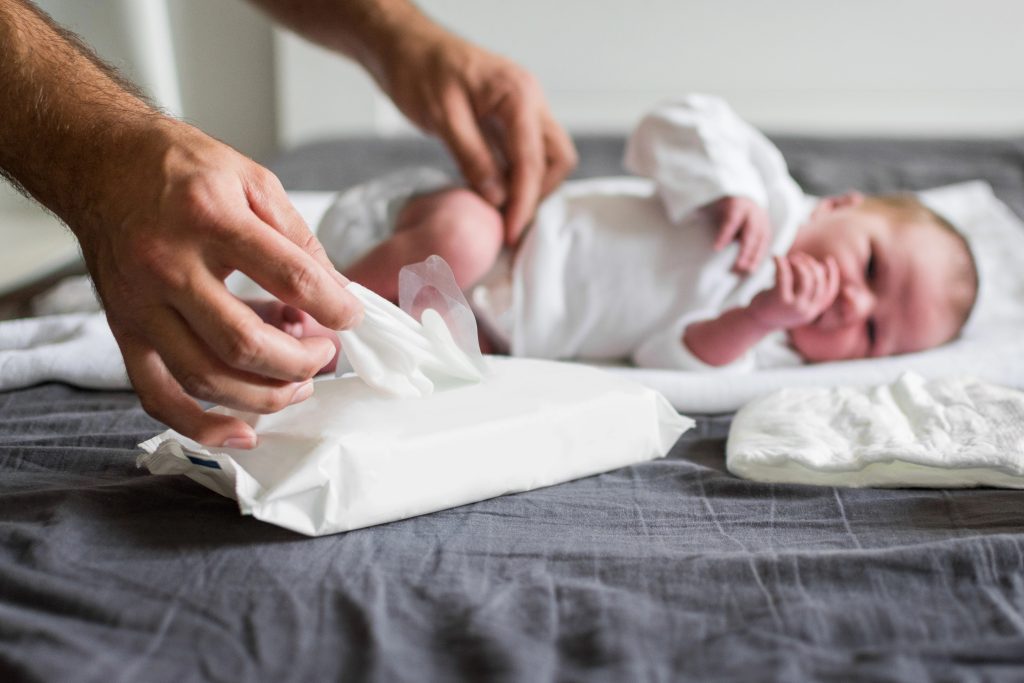 Father changing newborn baby's diaper and taking a wet wipe to clean the baby. Selective focus on wipes package and father's hand. Closeup, no retouch, natural lighting.