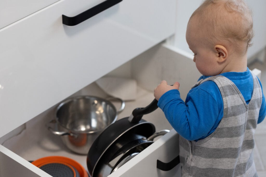 The baby with blond hair taking pan out from a kitchen drawer