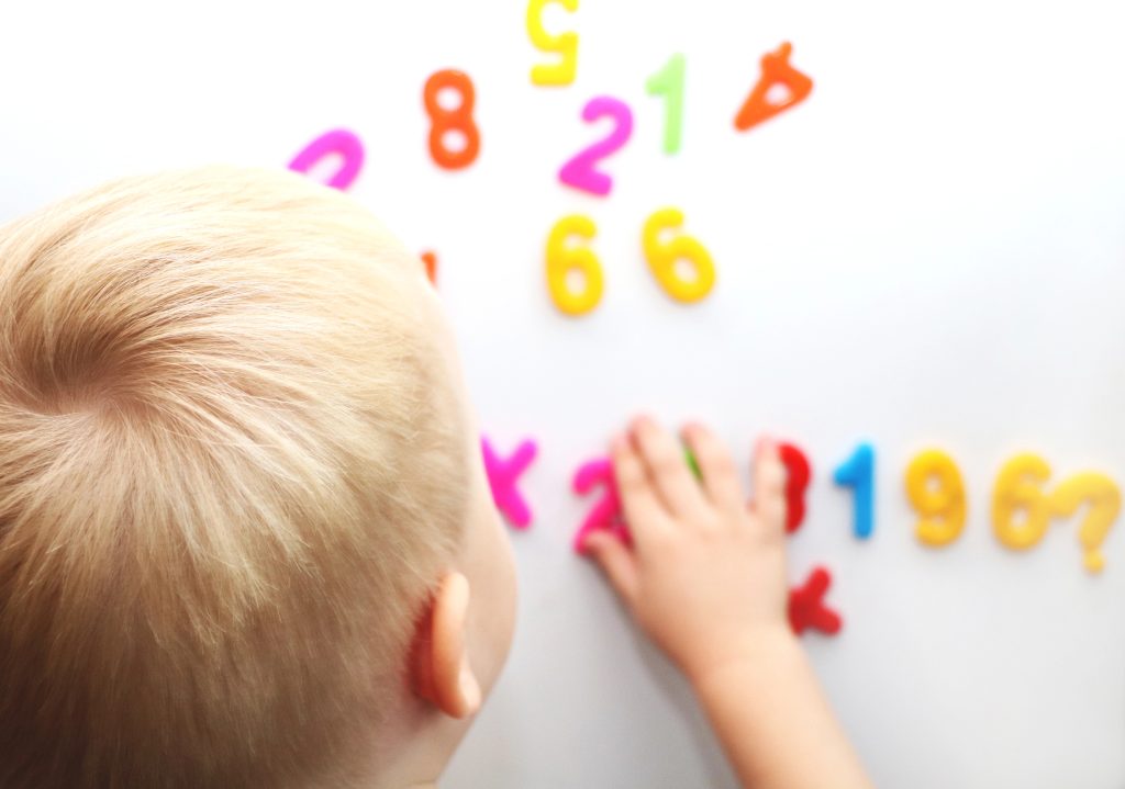 A little boy is studying the magnetic numbers on the fridge. Preschooler training