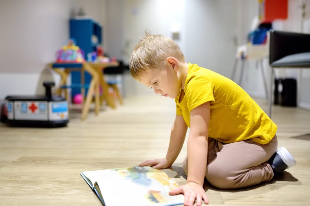 Cute little boy reading a book on the floor in a kindergarten. The child has an interesting time in the preschool