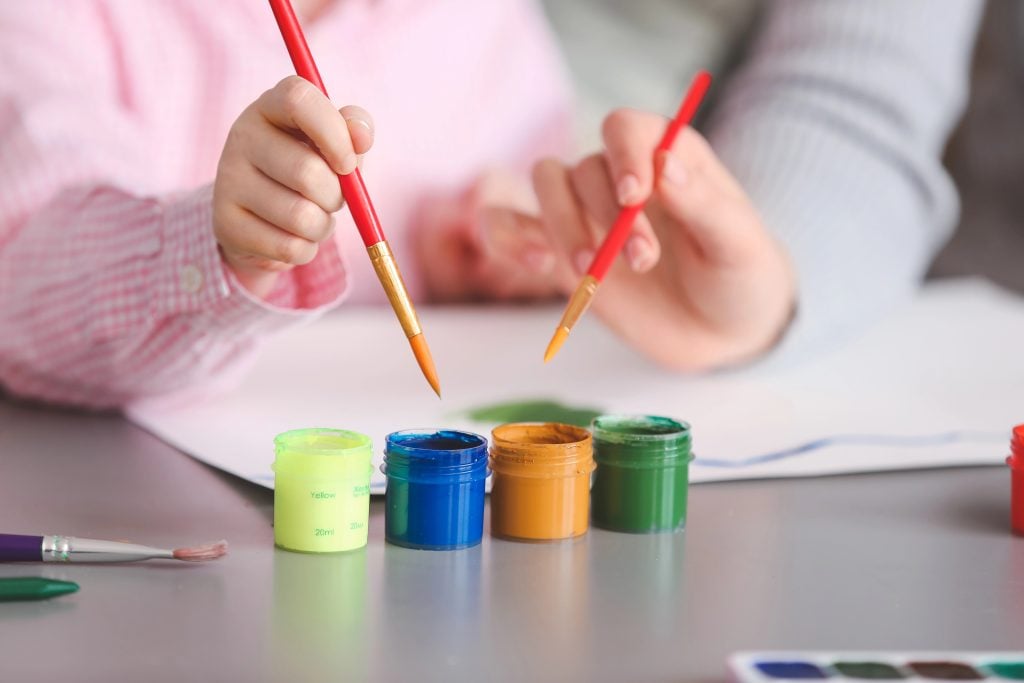 Drawing teacher giving private art lessons to little girl at home, closeup
