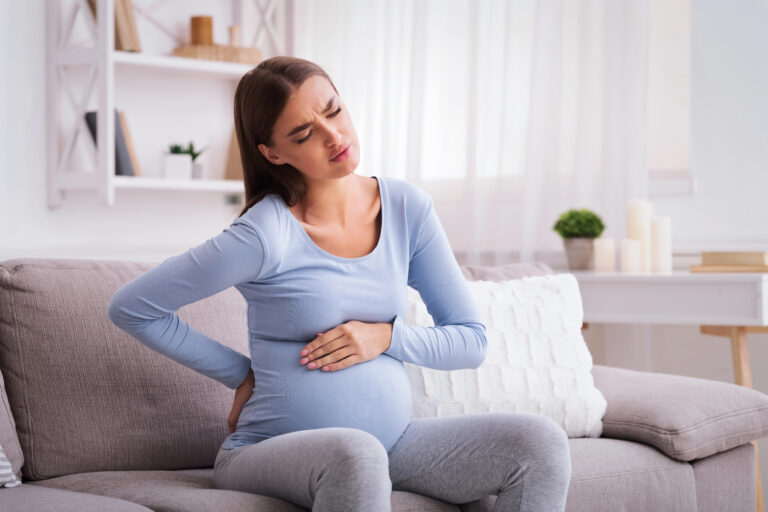 Pregnant Lady Having Backache Massaging Back Sitting On Sofa Indoor