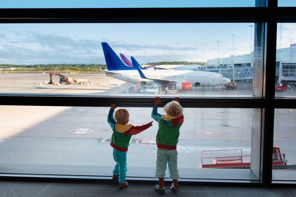 Kids at airport. Children look at airplane. Traveling and flying with child. Family at departure gate. Vacation and travel with young kid. Boy and baby before flight in terminal. Kids fly a plane.