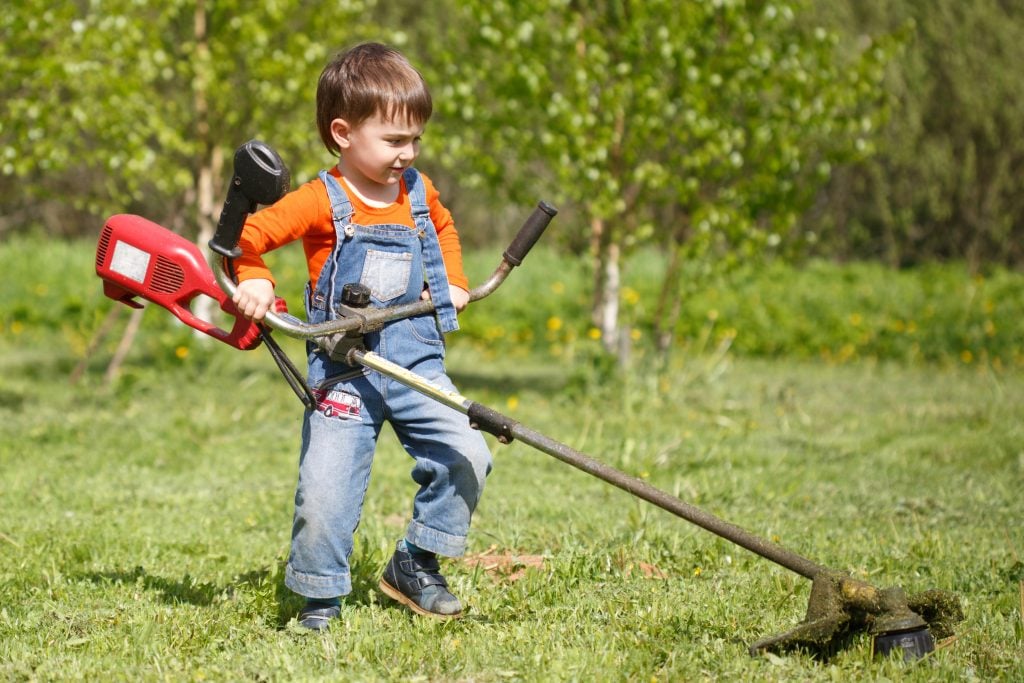A little boy mows the trimmer on the floor in a sunny summer day.