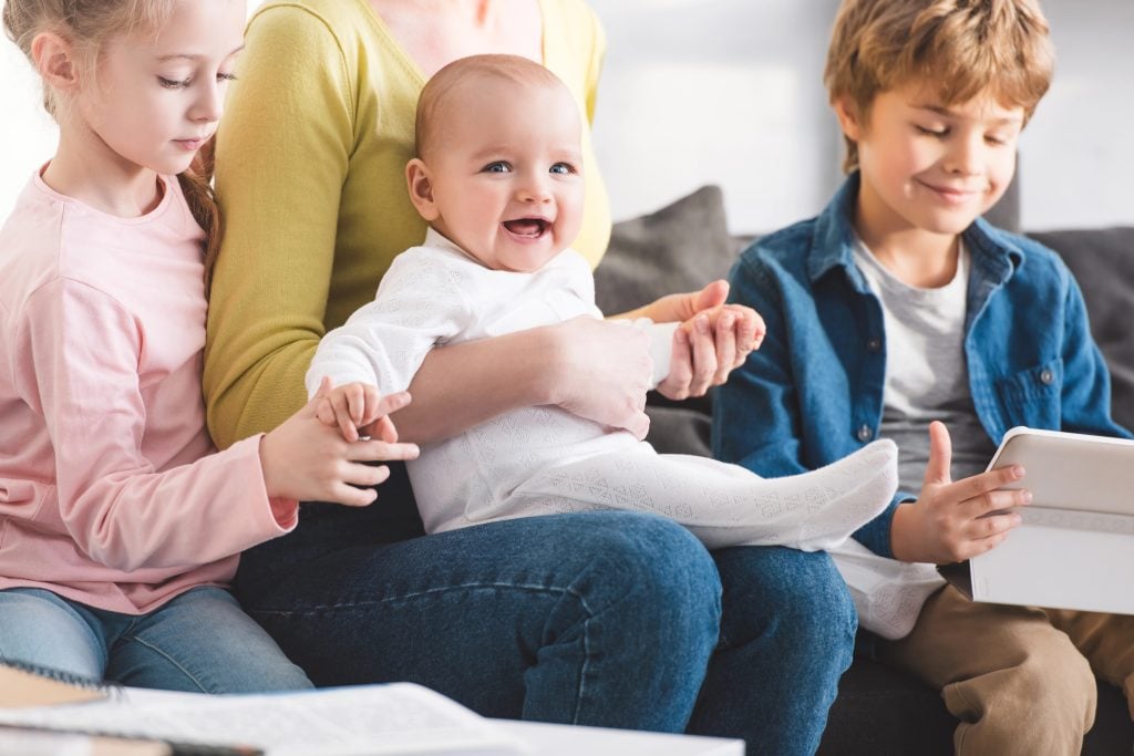 cropped shot of mother with infant child and cute siblings sitting together in sofa