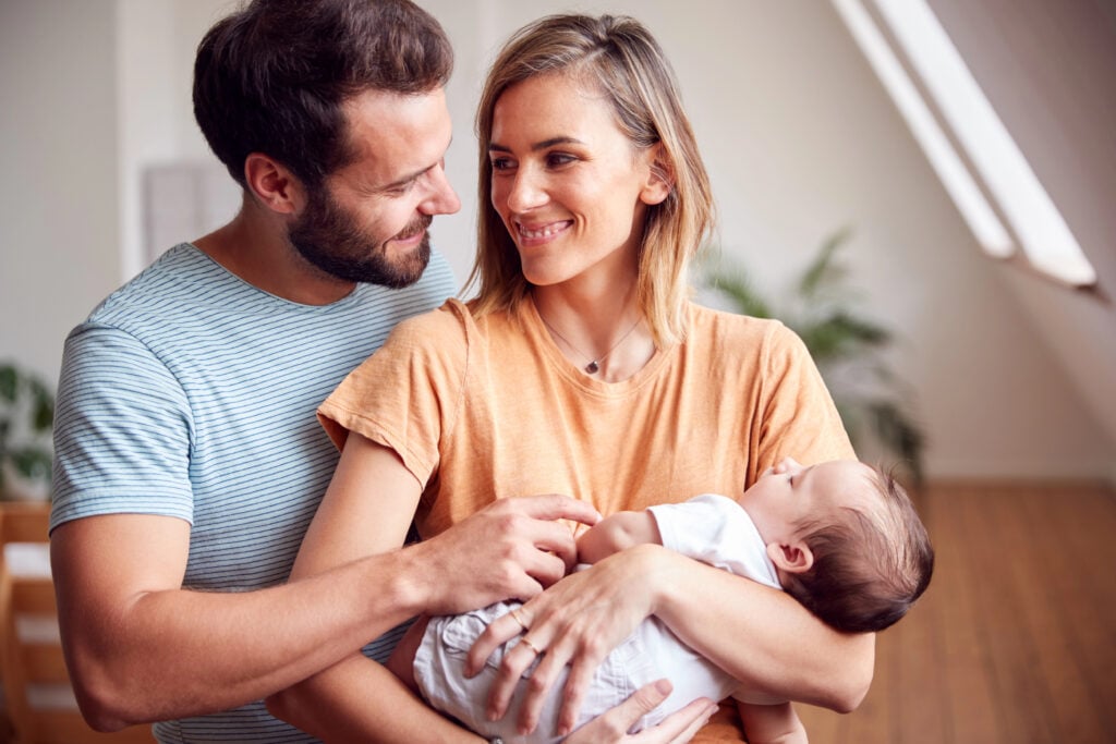 Loving Parents Holding Newborn Baby At Home In Loft Apartment