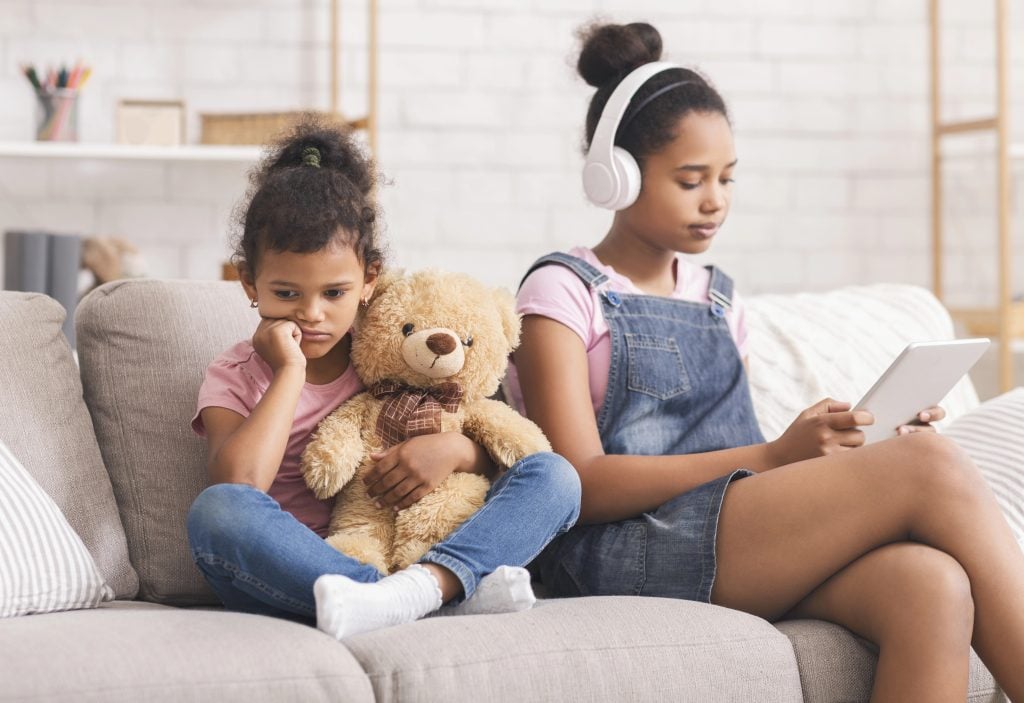 Little african girl boring alone, her elder sister watching videos