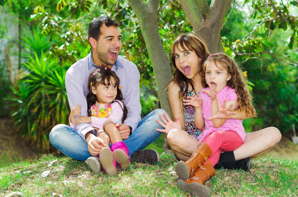 Beautiful hispanic family of four sitting outside on grass engaging in conversations while posing naturally and happily