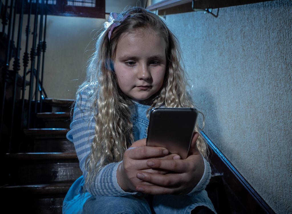 Sad depressed girl Bullied by text message humiliated online social media by classmates. Sad depressed young girl victim of cyberbullying by mobile phone sitting on stairs feeling lonely hopeless.