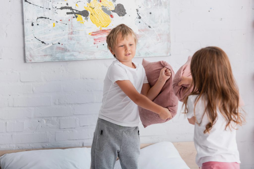 siblings in pajamas having fun while fighting with pillow in bedrooms