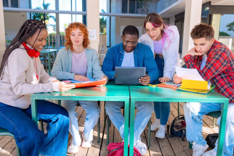 Five students with laptops and notes sit near the campus to review the exam.tudents with laptops sit near the campus and communicate.