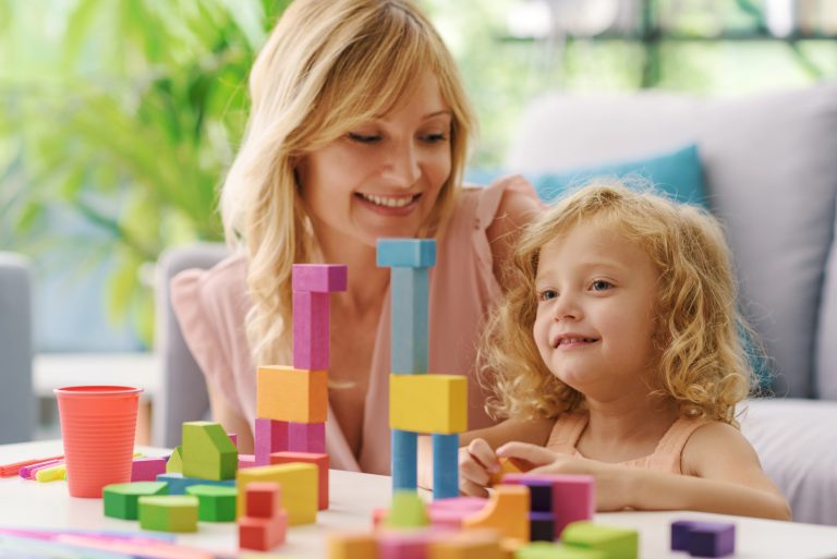 Happy cute girl with her mother in the living room, they are playing with wooden blocks