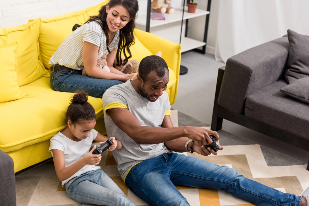 excited father and daughter playing video games while mother sitting on couch