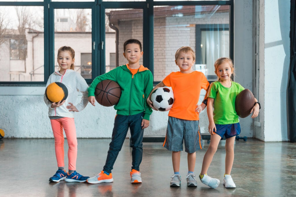 Front view of multiethnic children smiling and holding balls in gym