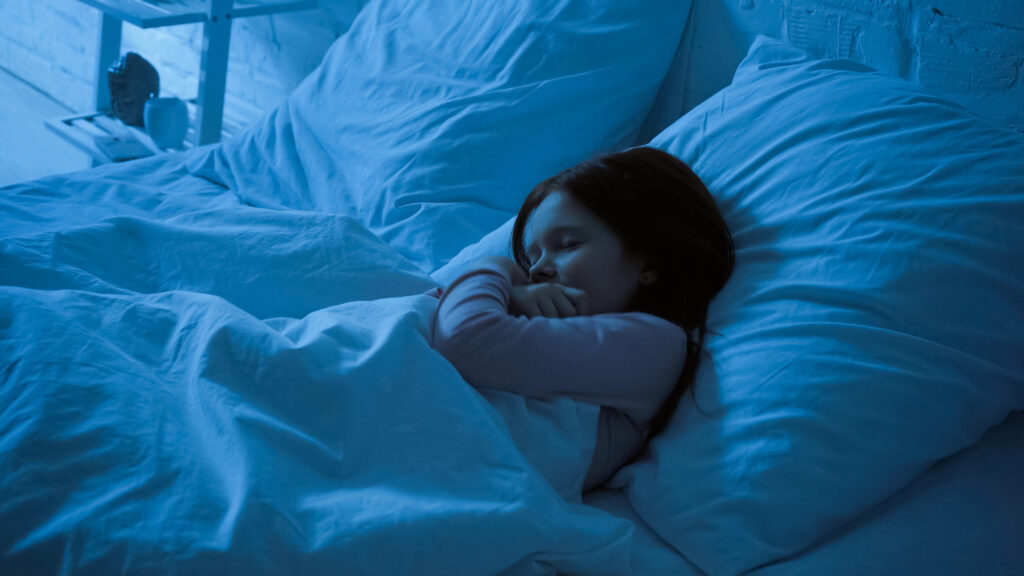 Preteen kid hugging blanket while sleeping on bed