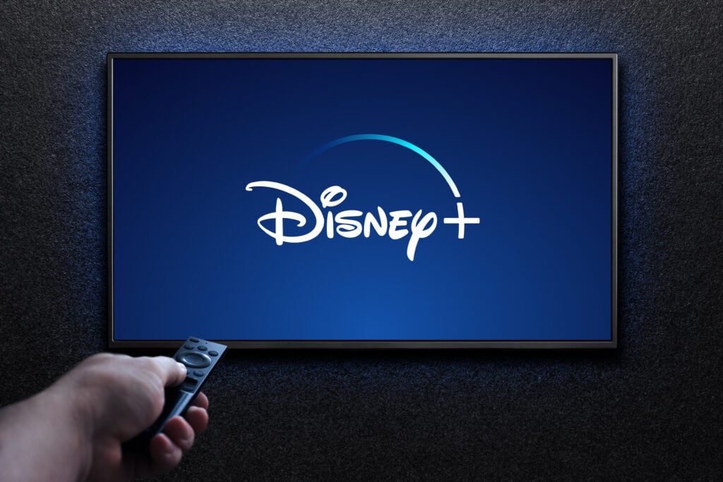 Disney plus logo on TV screen. Man turns on TV with remote control. Disney plus is an American subscription video streaming service. Astana, Kazakhstan - July 21, 2023.