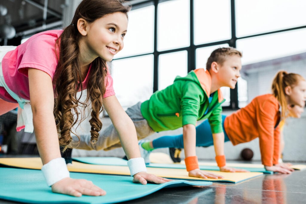 Smiling kids doing plank exercise on fitness mats