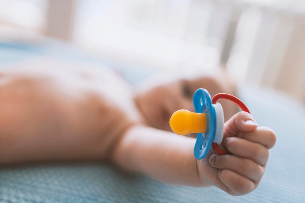 Baby with a nipple. Close up of baby hands with pacifier. Focus is on hands. Newborn sleeping on a blanket holding a pacifier in his hand. Baby is lying happy holding baby nipple soother in hand