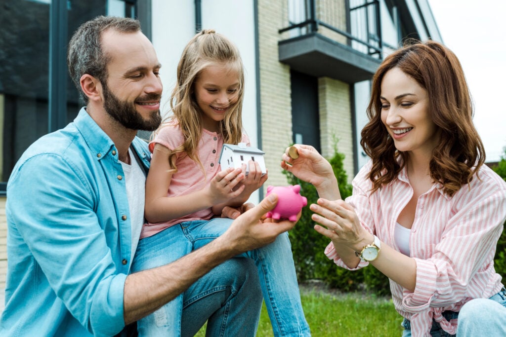 happy woman putting golden coin in piggy bank near husband and daughter