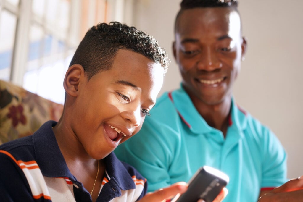 Father Teaching Mobile Telephone Technology To Son At Home