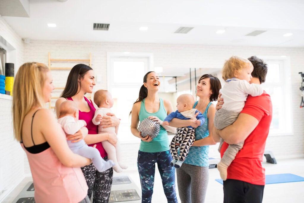 Group exercise class, mother working out with a baby in gym. Moms staying active while boding with babies. New parent friends.