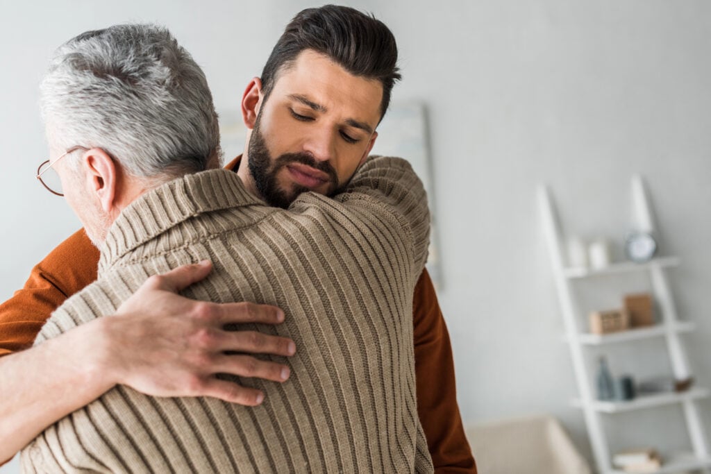 handsome bearded man hugging elder father at home